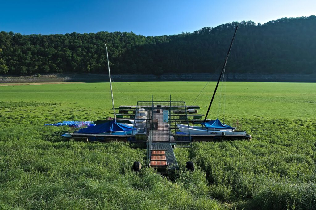 Segelboote liegen an einem Steg auf dem bewachsenen Speicherboden des Edersees