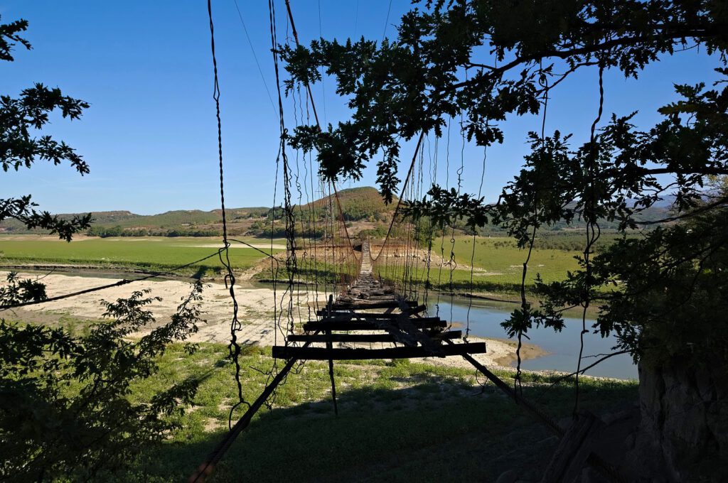 Blick entlang einer stark beschädigten Hängebrücke bei Bushkash mit fehlenden Holzbohlen, verformten Drahtseilen und rostigen Aufhängungen.